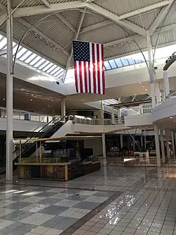 A large, two-level mall atrium with no visible shops or patrons. An American flag hangs from a rounded truss.