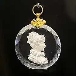 medallion with gold hook and white queen-looking woman encased in a circle of glass