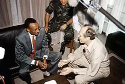 Overhead view of Kagame and Perry seated on leather seats with a large microphone visible and another army member in the background