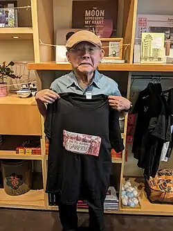 Daniel Tsang holds a t-shirt with a photo from a 1979 protest where he and others hold a banner that reads "We're Asians - Gay & Proud."
