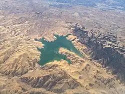 A reservoir with low water levels surrounded by dry, golden hills.