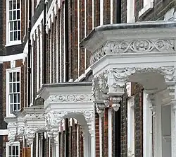 A row of ornate white porches hanging out from dark red brick houses.