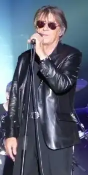 Jacques Dutronc singing on stage, wearing sunglasses and a dark jacket