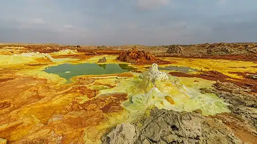 Image 7 Dallol Photograph credit: Alexander Savin Dallol is a cinder-cone volcano in the Danakil Depression, northeast of the Erta Ale Range in Ethiopia. The area lies up to 120&nbsp;m (390&nbsp;ft) below sea level, and has been repeatedly flooded in the past when waters from the Red Sea have inundated it. The Danakil Depression is one of the hottest places on Earth, and the evaporation of seawater after these flooding episodes produced thick deposits of salt, as seen in this landscape. The deposits at Dallol include significant quantities of the carbonate, sulfate and chloride salts of sodium, potassium, calcium and magnesium. Hot springs discharge brine to form the blueish ponds, and small, temporary geysers produce cones of salt. More selected pictures