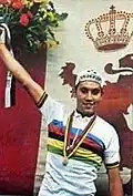 Eddy Merckx wearing a jersey with rainbow stripes, holding a bouquet of flowers.