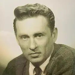 A greyscale photograph of Edmund Gettier, he is facing the camera, wearing a shirt, tie and cardigan.