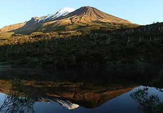 A small lake reflecting the view of a mountain in morning sunlight behind