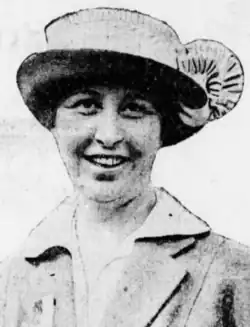 A white woman wearing a hat with a flat crown and a turned-up brim, and a soft suit over a blouse with a wide collar