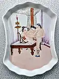 A Chinese porcelain plate, c. 1900, depicting a man having sexual intercourse with a woman with bound feet.