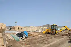A photo of several homes, made completely of wood and incomplete, being built. A yellow-and-black dozer is visible to the right of the homes.