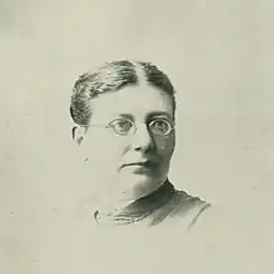 Portrait photo of a middle-aged woman wearing glasses with an up-do hairstyle parted in the center.