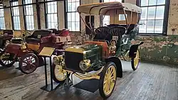 A green-colored, old-fashioned car with four seats and brass fittings