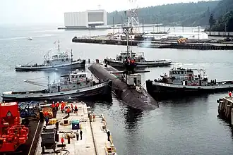 Naval Submarine Base Bangor with tug Mishawaka (rear left) and three other Natick-class tugs guiding the USS&nbsp;Ohio&nbsp;(SSGN-726) out of dry dock at Delta Pier