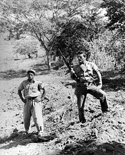 Frank Sturgis stands over a mass grave, after the San Juan Hill massacre. (January 12, 1959).