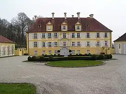 View of a large building with a yellow facade, behind a wide courtyard.