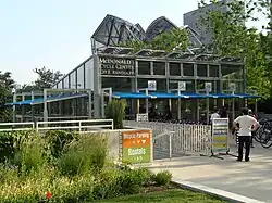 A glass building beyond landscaping with signs pointing to downstairs facilities and a sign reading "McDonald's Cycle Center 239 E. Randolph" with people in the building and in front of it