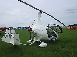 G-YFLI - Autogyro Cavalon on the grass at Dunkeswell. It is white, with one cockpit door open. It is very sleek and you can see a man stepping out.