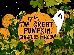 The words "It's the Great Pumpkin, Charlie Brown" written on a pumpkin with leaves around it and a ghost with black eyes behind it. Other pumpkins and the night sky can be seen in the background.