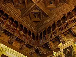 a view into then corner of a room done in carved wood with an arcade of columns and a ceiling of squares with roundels inside