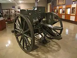 Colour photo of a green artillery gun inside the gallery of a museum. Other exhibits are visible behind the gun.