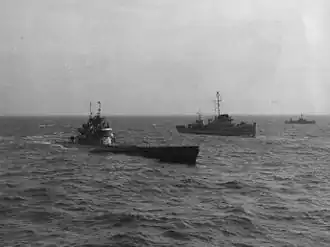 A submarine is in the foreground; to its right are two ships. Dione is to the left, and a smaller unknown ship is to the right