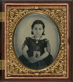 Girl in mourning dress holding framed photograph of her father, USA, encased, c. 1861–1870