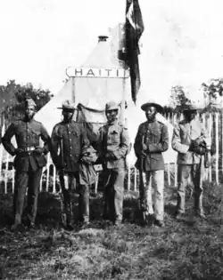 A group of five soldiers in front of a tent with a sign labeled "Haiti"