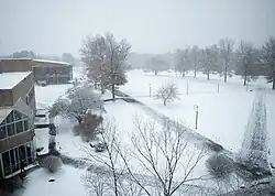 Snow is seen covering grassy areas, roofs on buildings, and trees at Hampshire College, a private liberal arts college in Massachusetts; sidewalks are also partially covered with snow