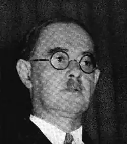 Photograph of a man with circular glasses and a toothbrush mustache