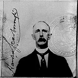 Black and white ID photo of tall-looking man with graying hair and mustache