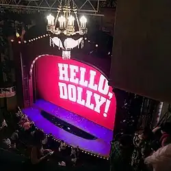 A stage with a pink screen reading "HELLO, DOLLY!" in white text.