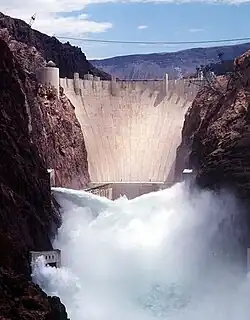 Front view of a dam in a narrow canyon, with water shooting out of the gates