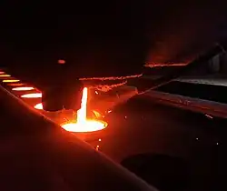 In-stream inoculation addition while molten cast iron is poured to a green sand mold in a foundry