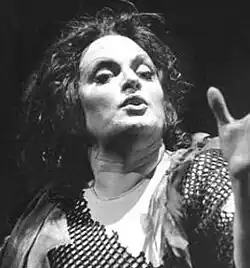 Black and white dramatic publicity shot of a performing female opera singer in stage make-up and big hair. Her head is uplifted, her mouth is open, and her hand is gesturing.