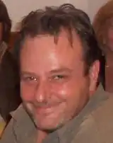 A portrait shot of a smiling, dark-haired man with dark brown eyes.