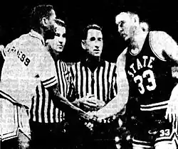 Black Loyola player Jerry Harkness and white Mississippi State player Joe Dan Gold shake hands in front of two referees.