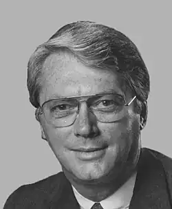 A color portrait of a gray-haired man in his seventies wearing a suit