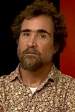 close-up image of João Miguel wearing a patterned shirt, looking sternly at camera