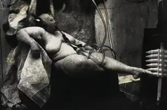 A black and white photograph of a different woman in a similar pose and styling as the first.