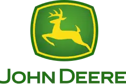 A green, rounded square with a yellow jagged outlines on the four sides of the square near the outside of its green border can be seen. In the middle of the yellow outline, a biological entity drawn outlined in yellow can be seen in a leaping position. This animal is commonly referred to as a deer. Underneath the deer and the green box, the words in small caps, 'JOHN DEERE' can be read.