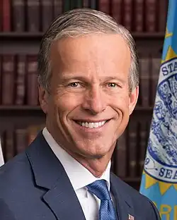 John Thune smiling in front of a South Dakota flag