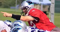 A photo of a helmeted football player pointing his finger while on a practice field