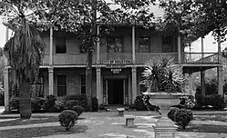 Brick two-storey gambral-roofed house with wraparound porch and second story balcony with columns. Square columns on first floor porch are of brick.