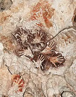 Le «&nbsp;Bouquet de mains&nbsp;», une manifestation remarquable de l’art rupestre de Bornéo, met en scène six mains dans une ronde graphique éternelle. A noter des mains de couleur rouge orangé plus anciennes recouvertes par le motif.