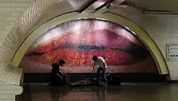 A mosaic inside a metro station showing an extreme close-up of a woman's red lips, two subway musicians in front