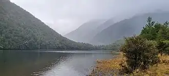 A lake with steep bush-covered mountains in the background