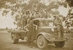 a black and white photograph of men in working clothes standing beside and on the back of a flatbed truck
