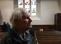 Portrait of elderly man in a church, backlit by a stained glass window