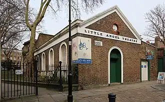Redbrick single storey building with white pediment, frieze at gutter level and arch topped shaping of windows and entrance with leafless trees against a light sky