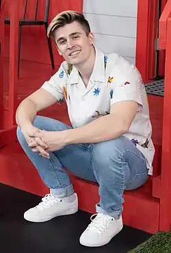 Full-body shot of Ahgren sitting anx wearing a white shirt with various patterns